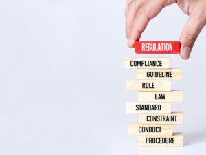 Hand stacking blocks labeled regulation and compliance.